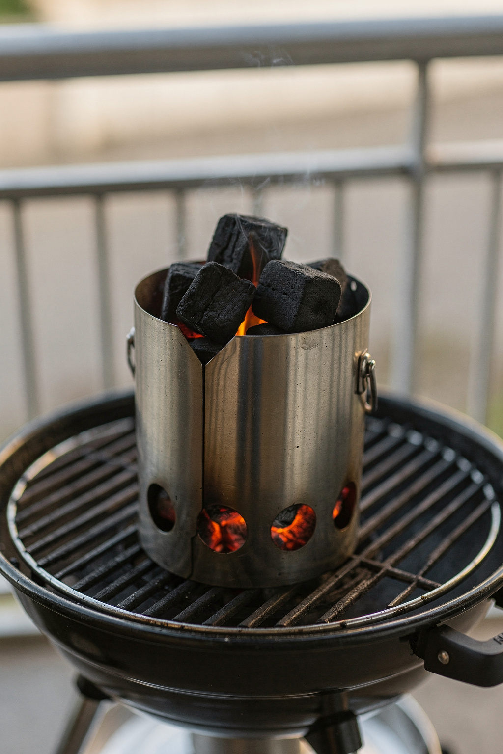 Holzkohle wird in einem kleinen Grillkamin angezündet, der auf einem Balkon steht.