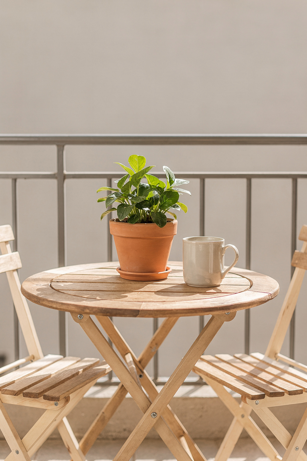 Kleiner Gartentisch aus Holz auf einem Balkon mit zwei Stühlen und einer Topfpflanze im Morgenlicht.