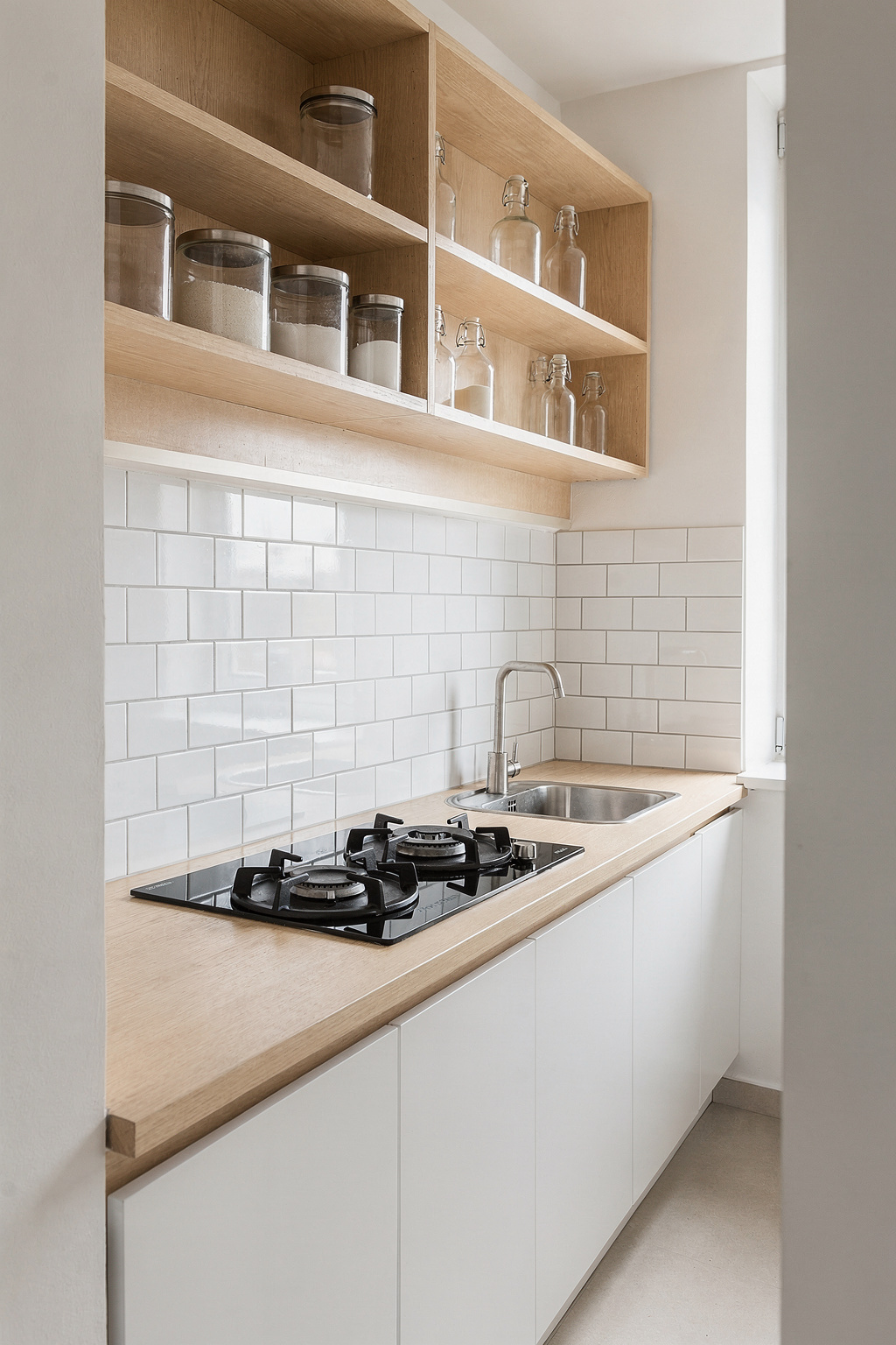 Eine schmale Küchenzeile in einer kleinen Wohnung mit Induktionskochfeld, Miniatur-Spüle und offenen Wandregalen.