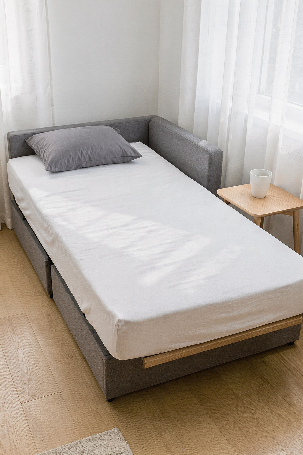 Kompaktes Sofa mit Bettfunktion in kleiner Wohnung, ausgeklappte Schlaffläche mit grauer Bettwäsche ohne Aufschrift.