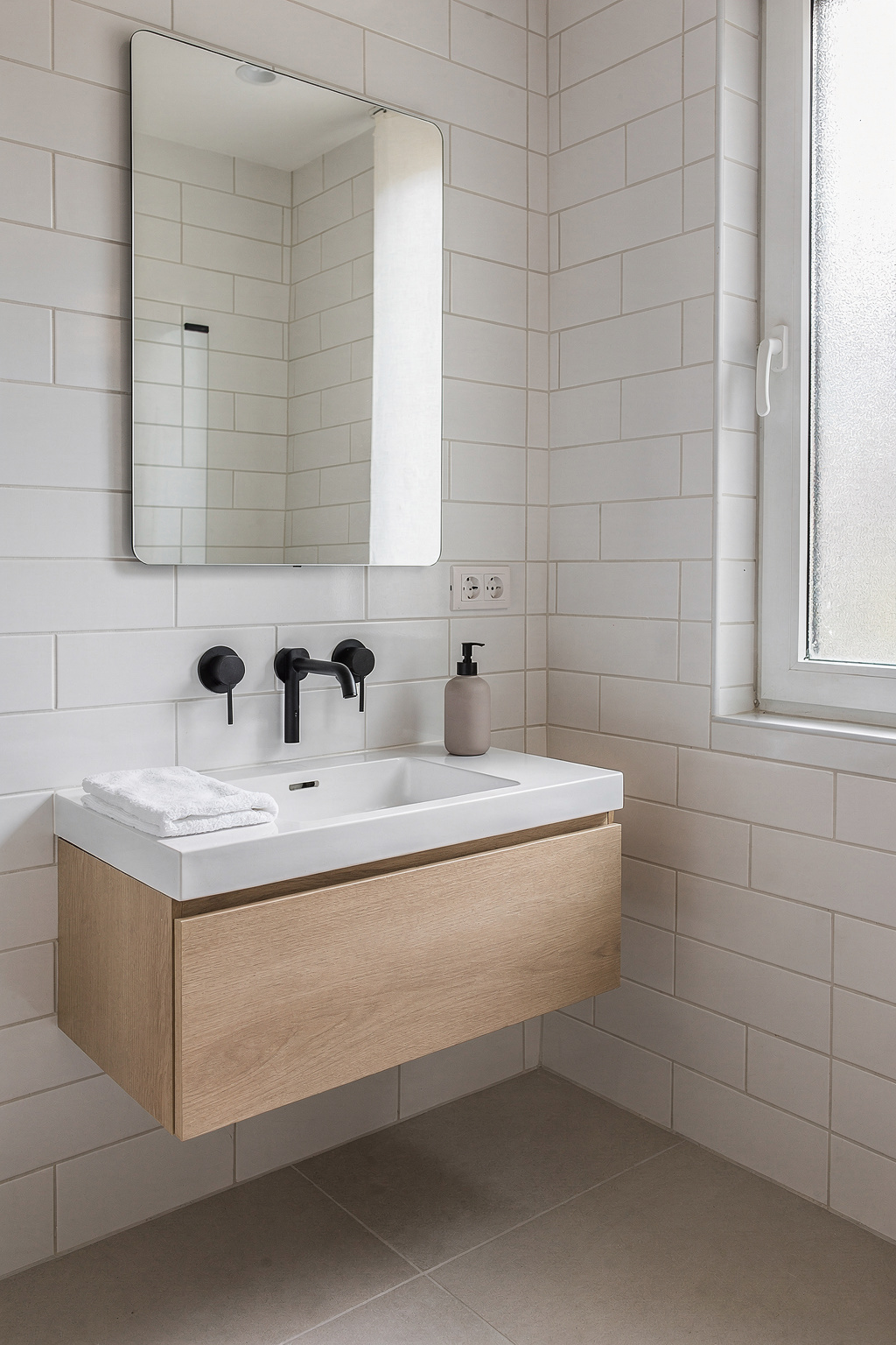 Modernes Badezimmer mit weißen Fliesen, schwarzen Armaturen und einem freistehenden Waschtisch in einer kleinen Erstwohnung.
