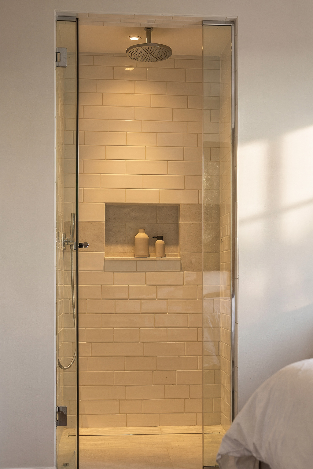 Schmale Dusche im Schlafzimmer mit Regenduschkopf und gefliester Nische, platzsparend eingebaut.