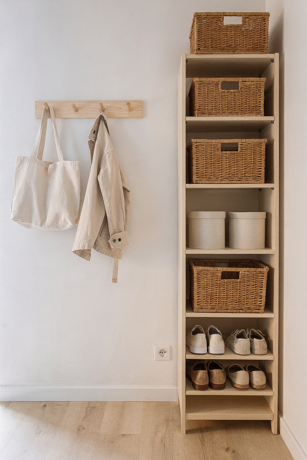 Ein schmales Eingangsregal mit Körben und Haken an der Wand einer kleinen Wohnung. Schuhe und Taschen sind ordentlich verstaut.