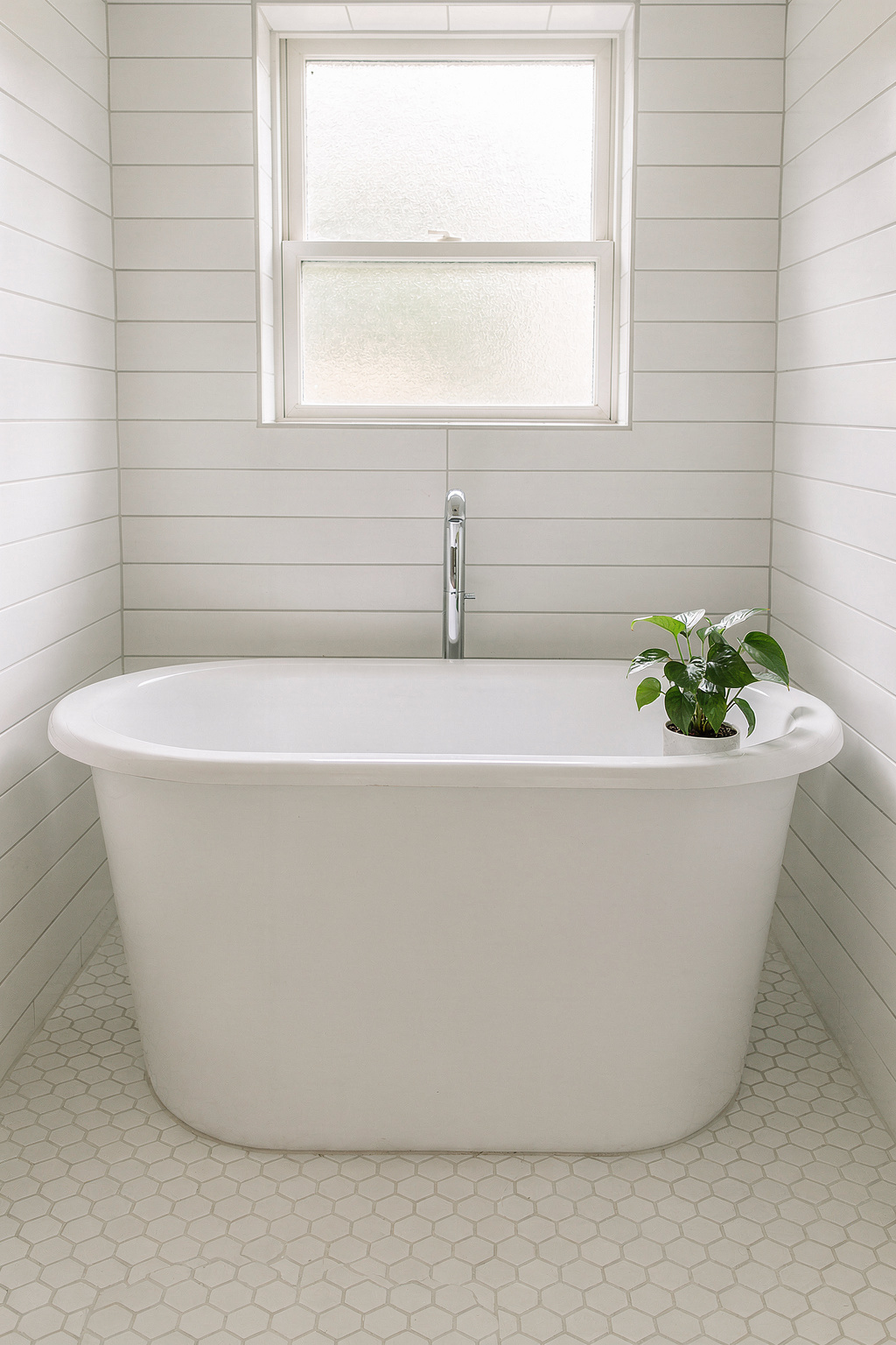Freistehende Badewanne in einem kleinen Bad mit hellem Licht und minimalistischer Einrichtung.
