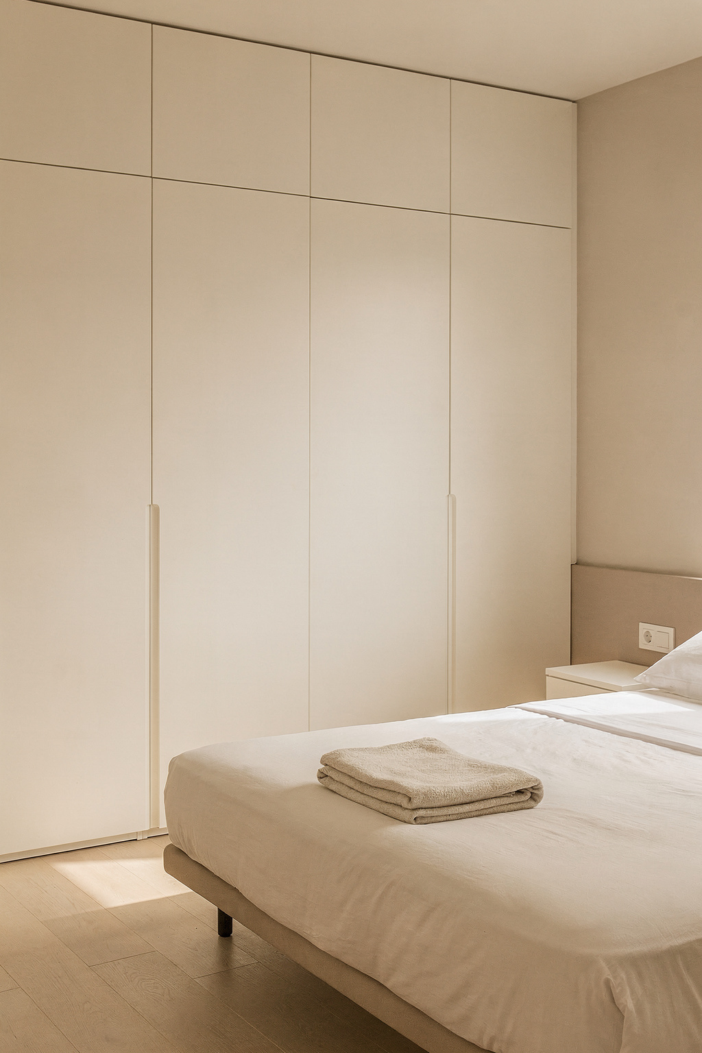 Schmales Schlafzimmer mit eingebautem Kleiderschrank und aufgeräumten, leeren Ablageflächen.