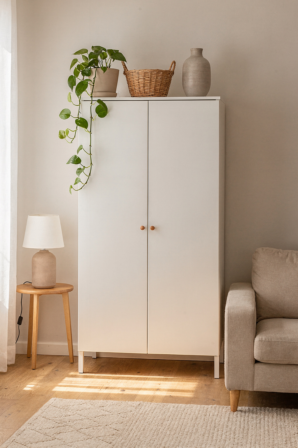Deko auf dem Schrank mit hängender Pflanze, Weidenkorb und kleiner Vase in einem hellen Wohnzimmer.