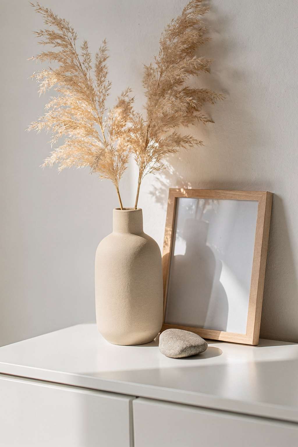 Kleine Schrank Deko mit Keramikvase, trockenem Pampasgras und einem schlichten Bilderrahmen in Nahaufnahme.