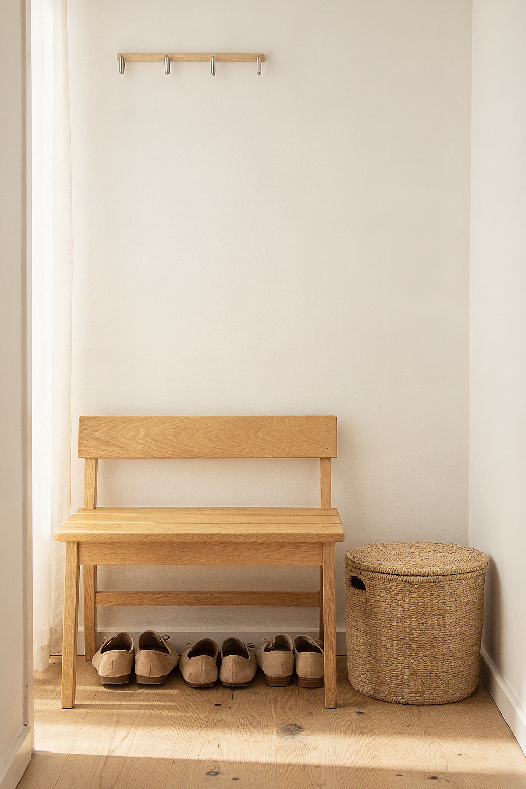 Eine Holzbank mit Lehne im Flur einer kleinen Wohnung, darunter Schuhe und ein geflochtener Korb zur Aufbewahrung.