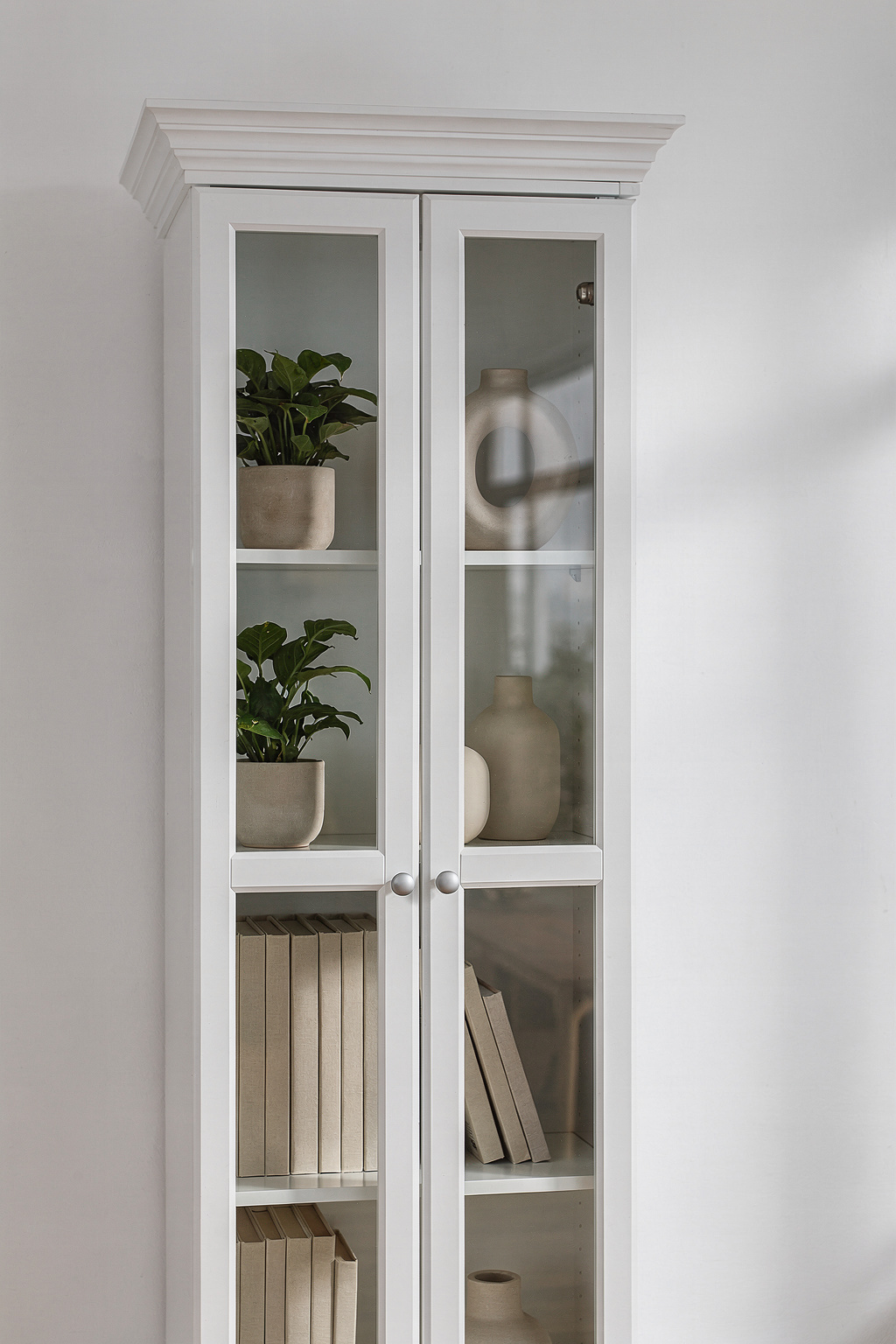 Ein IKEA Billy Regal mit aufgesetzter Zierleiste und Glastüren wirkt wie ein eingebautes Bücherregal. Pflanzen und Deko ergänzen den Look.