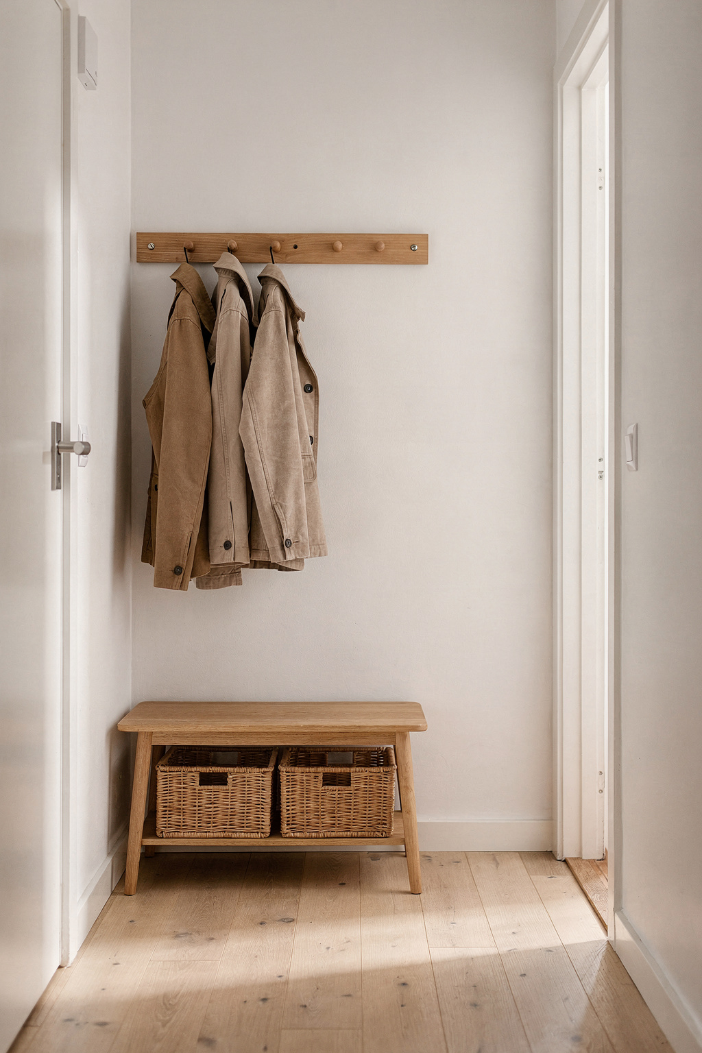 Eine schmale Garderobe im Flur mit wandmontierter Hakenleiste und kleiner Sitzbank aus hellem Holz.