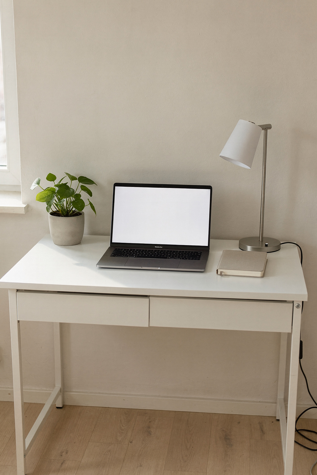 Ein aufgeräumter Home Office Arbeitsplatz mit weißem Schreibtisch, Laptop und kleiner Pflanze am Fenster.