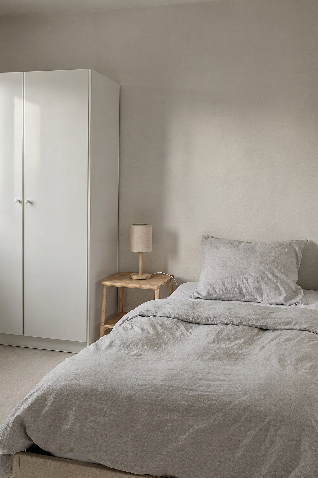 Schmales Schlafzimmer mit Einzelbett, weißem Kleiderschrank und kleinem Nachttisch für eine erste Wohnung.