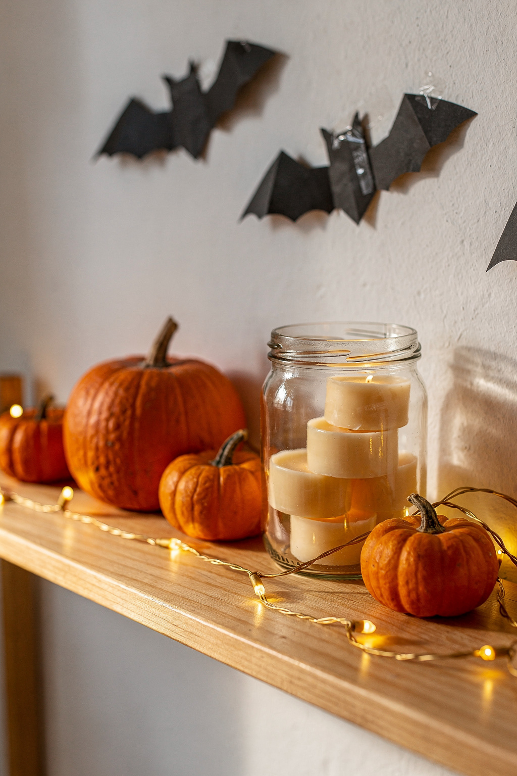 Günstige Halloween Deko: kleine Kürbisse und DIY Papierfledermäuse auf einem Holzregal in einer Studentenwohnung.