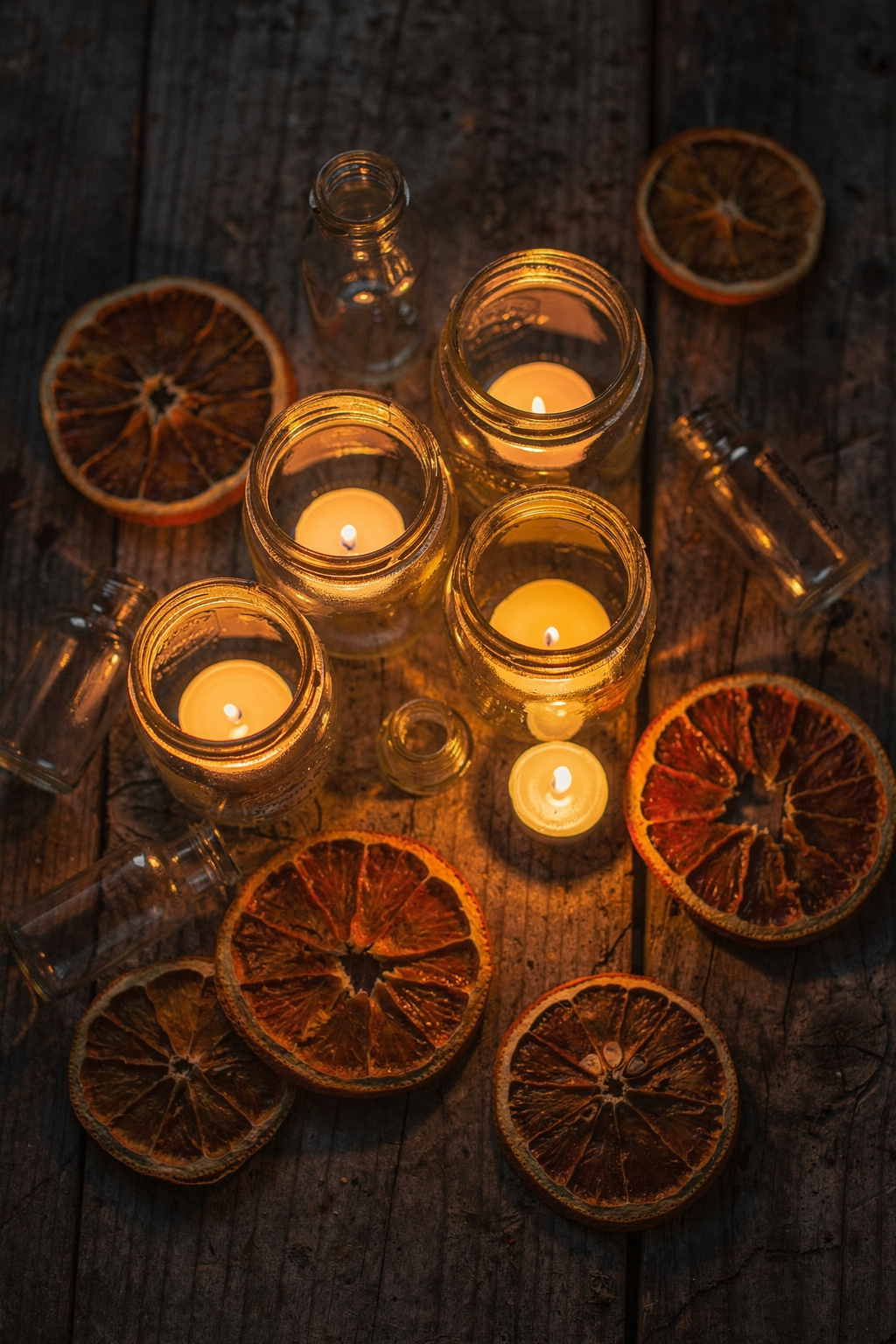 Kleine Einmachgläser mit Kerzen und getrockneten Orangenscheiben als selbst gemachte Halloween Deko auf einem Holztisch.