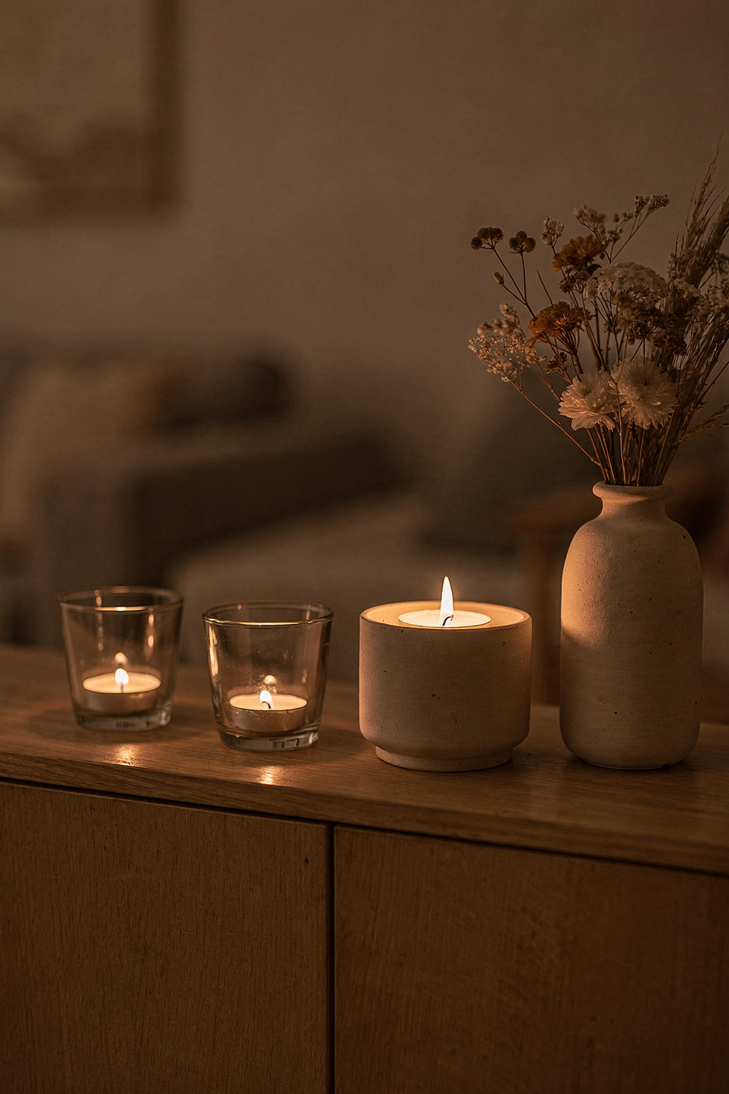Kerzen Deko im Wohnzimmer mit Glasvasen und getrockneten Blumen auf einem Sideboard kombiniert.