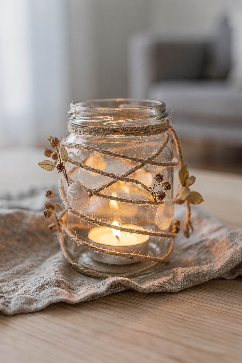 Windlicht aus einem leeren Einmachglas, umwickelt mit Juteschnur und kleinen Muscheln als Dekoration.